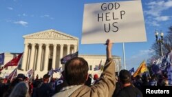 ARHIVA - Čovek drži parolu "Bože, pomozi SAD" tokom protesta zbog izbornih rezultata, ispred zgrade Vrhovnog suda SAD u Vašingtonu, 12. decembra 2020.