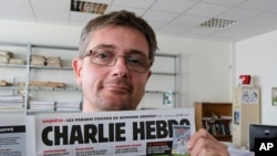 讽刺漫画刊物《查理周刊》发行总监在巴黎展示期刊头版，（2012年9月19日资料图）