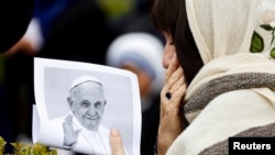 A person holds a picture of Pope Francis near the statue of late Pope John Paul II outside Gemelli Hospital where Pope Francis is admitted to continue treatment, in Rome, Italy.