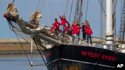 Para remaja Belanda, peserta pelayaran trans-Atlantik di masa karantina pandemi corona, bersorak di atas kapal mereka "Wylde Swan" setibanya di pelabuhan Harlingen, Belanda utara, Minggu, 26 April 2020. (Foto AP / Peter Dejong)