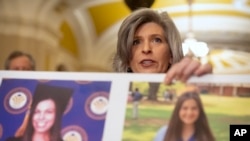 Sen. Joni Ernst, R-Iowa, holds a poster with photos of murder victims Sarah Root and Laken Riley as she speaks after a policy luncheon on Capitol Hill, Feb. 27, 2024, in Washington.