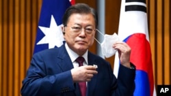 South Korean President Moon Jae-in removes his mask as he witnesses a signing ceremony at Parliament House, in Canberra, Australia, Dec. 13, 2021.