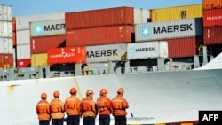 在美中两国开打贸易战的阴影下，中国工人站在山东省青岛港的一艘集装箱船旁(2018年4月8日)