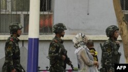 China -- A Chinese paramilatary police patrol passes a Muslim ethnic Uighur woman and a child on a street in Urumqi, capital of China's Xinjiang region on July 3, 2010.