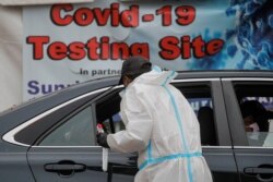 A healthcare worker takes a swab from a person sitting in a car at a drive-thru COVID-19 test center in Newark, New Jersey, Nov. 12, 2020.