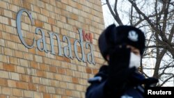 在加拿大驻北京大使馆外一名中国警察向摄影记者打禁止的手势。（2018年12月12日）