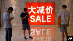 FILE - Chinese shoppers stand near a sale advertisement at a shopping area in Beijing, China, July 10, 2016.