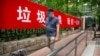 A man wearing a face mask to protect against the spread of the new coronavirus walks past a propaganda banner encouraging people to sort their garbage in Beijing, June 24, 2020.