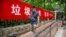 A man wearing a face mask to protect against the spread of the new coronavirus walks past a propaganda banner encouraging people to sort their garbage in Beijing, June 24, 2020.