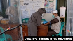 Seorang petugas medis yang mengenakan alat pelindung mengambil sampel darah dari seorang anggota Jamaah Tabligh untuk dites virus corona, Temanggung, Jawa Tengah, 20 April 2020. (Foto: Antara/Anis Efizudin via Reuters)