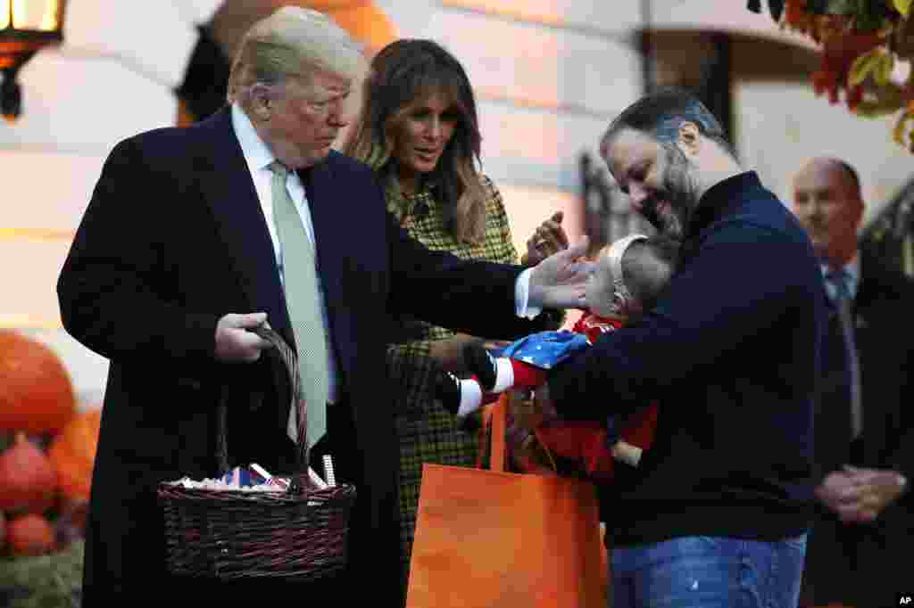 白宫万圣节活动中,家长抱着孩子领取总统唐纳德·特朗普和第一夫人梅拉尼娅·特朗普发的糖果(2018年10月28日)。