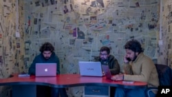 FILE- Fahad Shah, right, editor-in-chief of Kashmir Walla, works on his computer inside the newsroom at his office in Srinagar, Indian controlled Kashmir, Friday, Jan. 21, 2022. 