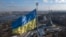 Ukraine's national flag, topped with a trident symbol, flutters above the capital with the Motherland Monument on the right, in Kyiv, Feb. 13, 2022.