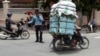 A Cambodian man, right, drive his motorbike overloaded with vegetable sacks as he passes a traffic police officer, center, in Phnom Penh, Cambodia, Tuesday, Aug. 25, 2015. (AP Photo/Heng Sinith)