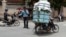 A Cambodian man, right, drive his motorbike overloaded with vegetable sacks as he passes a traffic police officer, center, in Phnom Penh, Cambodia, Tuesday, Aug. 25, 2015. (AP Photo/Heng Sinith)