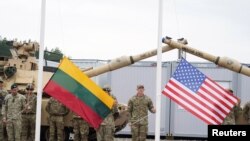 Para tentara bersiap mengibarkan bendera AS dan Lithuania dalam upacara pembukaan kamp tentara AS di Pabrade, Lithuania, pada 30 Agustus 2021. (Foto: Reuters/Janis Laizans)