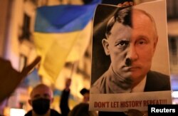 Seseorang memegang spanduk dengan wajah bergabung dari potret Vladimir Putin dan diktator Nazi Adolf Hitler selama protes anti-perang, setelah Presiden Rusia Vladimir Putin mengizinkan operasi militer besar-besaran terhadap Ukraina, di Barcelona, Spanyol, 24 Februari 2022. (Foto: REUTERS/Nacho Doce)