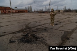 A Ukrainian soldier observes the place where a bomb fell, killing a fellow soldier not far from the front line in eastern Ukraine, Feb. 19, 2022, in Novoluganske. (Yan Boechat/VOA)
