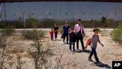 រូបឯកសារ៖ គ្រួសារមួយមានគ្នាប្រាំនាក់ដែលអះអាងថាមកពីហ្គាតេម៉ាឡា និងបុរសម្នាក់ដែលបញ្ជាក់ថាគាត់មកពីប្រទេសប៉េរូ ពាក់អាវពណ៌ផ្កាឈូក ដើរកាត់វាលខ្សាច់បន្ទាប់ពីឆ្លងកាត់ព្រំដែនអាមេរិកនិងម៉ិកស៊ិក ថ្ងៃអង្គារ ទី២៩ ខែសីហា ឆ្នាំ២០២៣។