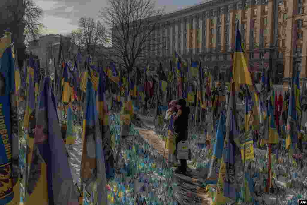 Visitors stand next to a makeshift memorial paying tribute to Ukrainian and foreign fighters with flags at the Independence Square in Kyiv ahead of the third anniversary of Russia's invasion of Ukraine.