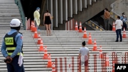 A medic (2nd L) wearing personal protective equipment (PPE) talks to a woman waiting to take a Covid-19 coronavirus test at the National Olympic Stadium in Phnom Penh on February 23, 2021. (Photo by TANG CHHIN Sothy / AFP)
