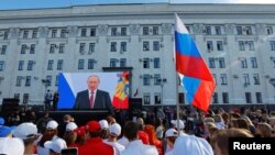 Sejumlah warga berkumpul di dekat layar besar yang menampilkan Presiden Rusia Vladimir Putin dalam acara deklarasi pencaplokan sejumlah wilayah Ukraina oleh Rusia di Luhanks, wilayah Ukraina yang dikontrol oleh Rusia, pada 30 September 2022. (Foto: Reuters/Alexander Ermochenko)
