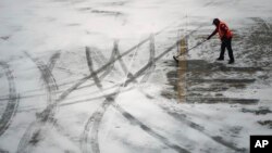 A worker clears snow from an apron before guiding a Delta Air Lines jet at the Detroit Metropolitan Wayne County Airport in Romulus, Mich., Jan. 6, 2025.