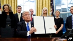 川普总统在白宫椭圆形办公室展示一项签过名的总统行政令。（2017年1月28日）