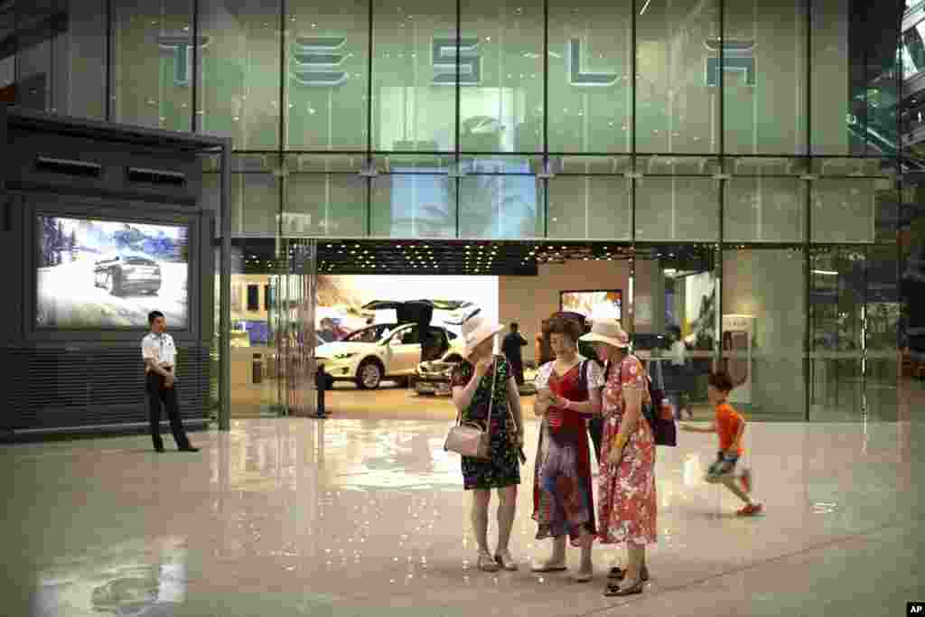 2018年7月5日，一些女士在北京一家高档购物中心的特斯拉展厅外观看智能手机。在美中关税之战中， 中国对包括特斯拉在内的一些美国公司的产品征收25%的关税。为了平衡这次关税增加，特斯拉提升了在中国市场的汽车售价。2017年，中国市场上销售的载人电能车辆增加了82%，达到47万辆，是美国同期销售量的两倍。