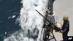 资料图片：2023年5月19日星期五，一名美国海军水手在霍尔木兹海峡的保罗·汉密尔顿号航空母舰上的机枪旁站岗。 (美联社图片)