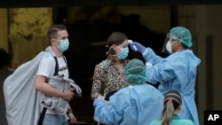 Petugas kesehatan yang mengenakan pakaian pelindung memeriksa suhu tamu di Hotel H10 Costa Adeje Palace di La Caleta, di Pulau Canary Tenerife, Spanyol, Jumat 28 Februari 2020. (Foto: AP)