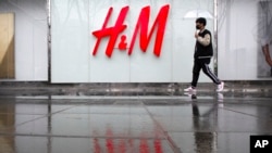 Seorang pria membawa payung berjalan melewati toko pakaian H&M di sebuah pusat perbelanjaan di Beijing, Jumat, 26 Maret 2021. (Foto: AP)