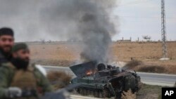 Syrian opposition fighters drive past a burning government armored vehicle south of Hama, Syria, on Dec. 7, 2024.