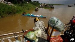 A vendor, foreground, stands on a ferry together with his goods before crossing the Mekong river in Dei Edth village at the outskirt of Phnom Penh, Cambodia, Wednesday, July 22, 2020. (AP Photo/Heng Sinith)