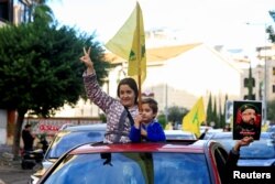 Žena pokazuje znak pobede zajedno sa detetom koje drži zastavu Hezbolaha, na ulazu u južno predgrađe Bejruta, nakon što je prekid vatre između Izraela i grupe Hezbolah stupio na snagu, Liban, 27. novembar, 2024. (Foto: REUTERS/Thaier Al-Sudani)