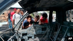 在巴格达萨德尔城一处热闹的露天旧家具市场外的爆炸现场，男孩查看一辆被炸毁汽车。(2021年4月15日)