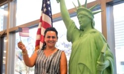 FILE - New US citizen Doris Nazarian waves the flag while posing beside a replica of the Statue of Liberty during a naturalization ceremony ahead of World Refugee Day by the US Citizenship and Immigration Services on June 17, 2021 in Los Angeles.