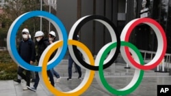 Warga yang mengenakan masker berjalan dekat Cincin Olimpiade di Stadion Nasional di Tokyo, Jepang (foto: dok). 