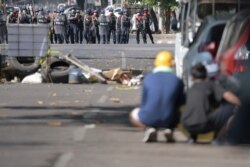 Demonstrators take shelter behind a barricade and some vehicles as riot police officers stand in front of them during a protest against the military coup in Yangon, Myanmar, March 1, 2021.