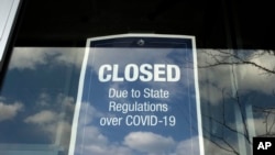 在马萨诸塞州戴德姆的一个露天商场，一家商店的橱窗上贴着一个关闭的告示（2020年4月22日）。