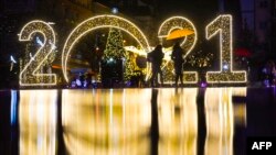 Žena sa kišobranom hoda ispred znaka 2021, pred proslavu Nove godine u Prištini, tokom trajanja pandemije koronavirusa, 30. decembra 2020. (Foto: Armend Nimani)