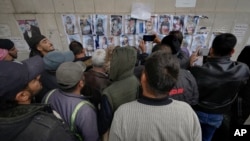 People examine photos as they search for missing or deceased people on the wall outside the morgue of Al-Mojtahed Hospital in Damascus, Syria, Dec. 11, 2024.