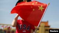 一名站在北京天安门广场的小男孩身穿美国T恤手拿中国国旗。（2019年5月7日）