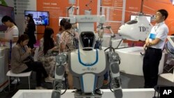 FILE - Visitors to the 21st China Beijing International High-tech Expo look at robots and helicopter drone displayed in Beijing, China, May 17, 2018. 
