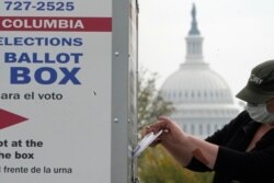 FILE - With the U.S. Capitol dome visible, a voter drops a ballot into an early voting drop box, at Union Market in Washington, Oct. 28, 2020.
