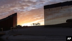 FILE - A pair of migrant families pass through a gap in the border wall to reach the United States after crossing from Mexico to Yuma, Ariz., to seek asylum, June 10, 2021.
