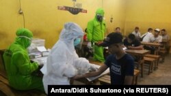 Petugas medis yang mengenakan alat pelindung mengambil sampel darah dari pengunjung yang dites virus corona di Surabaya, provinsi Jawa Timur, 18 April 2020. (Foto: Antara/Didik Suhartono) via Reuters)