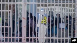 身穿防护服的工作人员看着从海外抵达北京的旅客进入北京国际会展中心等待接受进一步的健康甄别。（2020年3月18日）