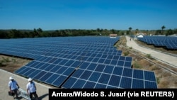 Pejabat PLN berjalan di dekat panel sel surya di pembangkit listrik tenaga surya terbesar di Desa Oelpuah, Kupang, 20 Juli 2017. (Foto: Antara/Widodo S. Jusuf via Reuters)