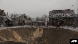 Pekerja komunal berjalan di samping kawah dan rumah-rumah yang hancur akibat serangan Rusia di Kyiv, 11 Desember 2023. (Roman PILIPEY / AFP)